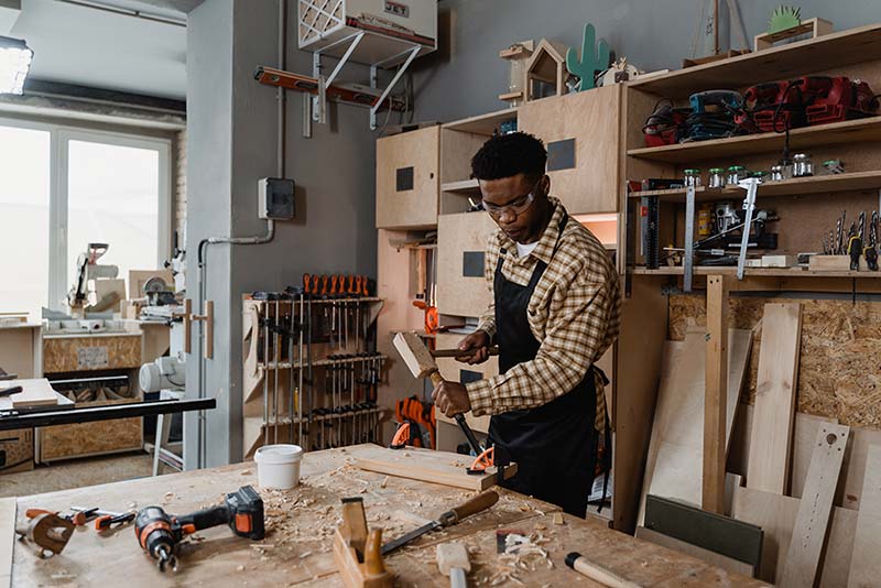 jeune menuisier qui taille dans du bois avec des outils